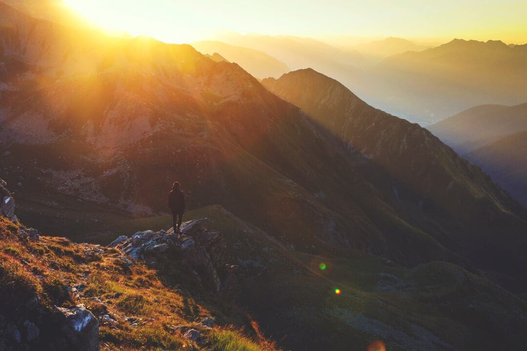 A person standing on top of a mountain at sunset.