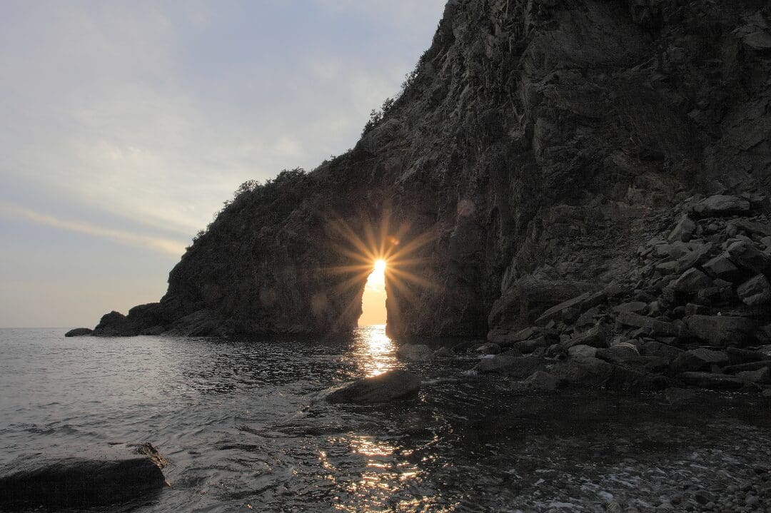 A sun is setting over the water and rocks.