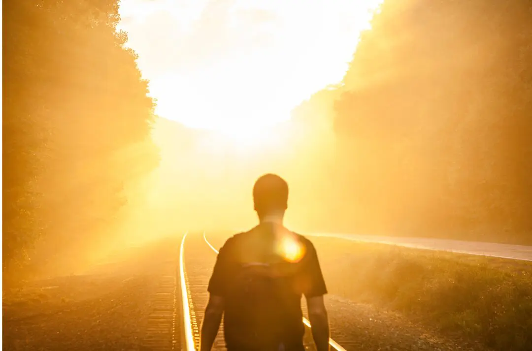 A man standing on the side of a road in front of a bright light.