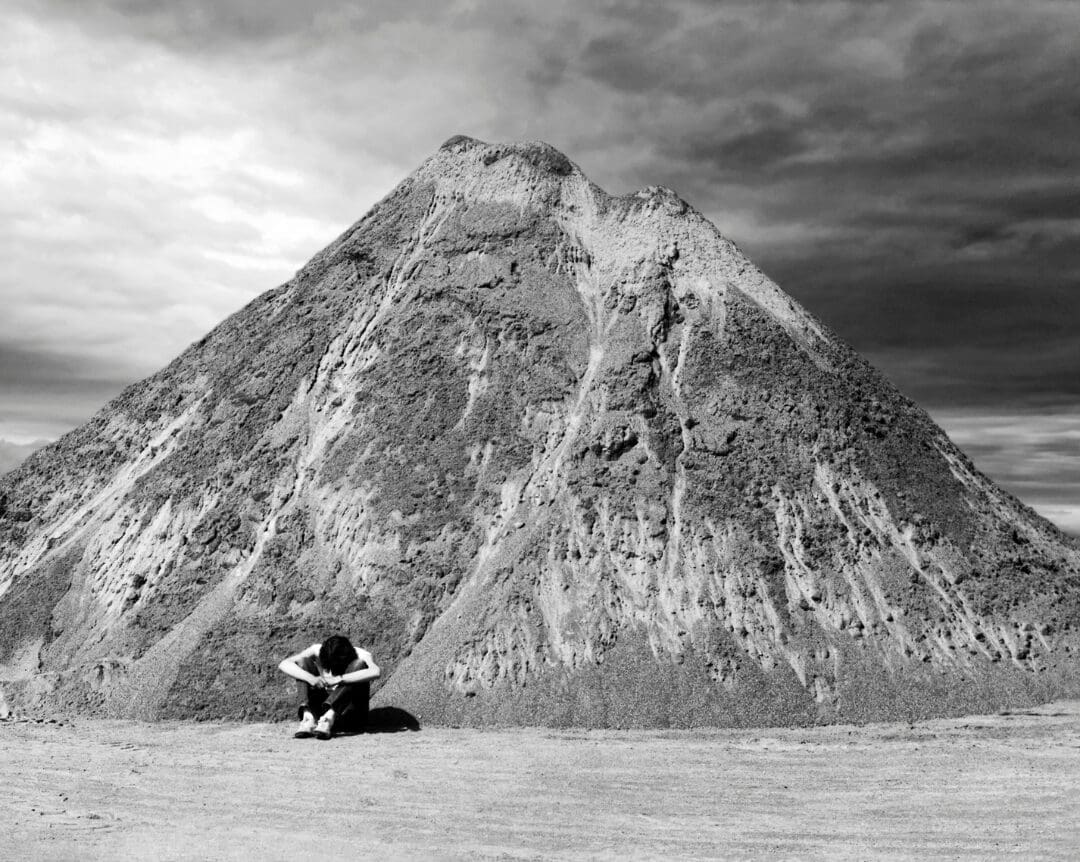 A person sitting in front of a mountain under cloudy skies.